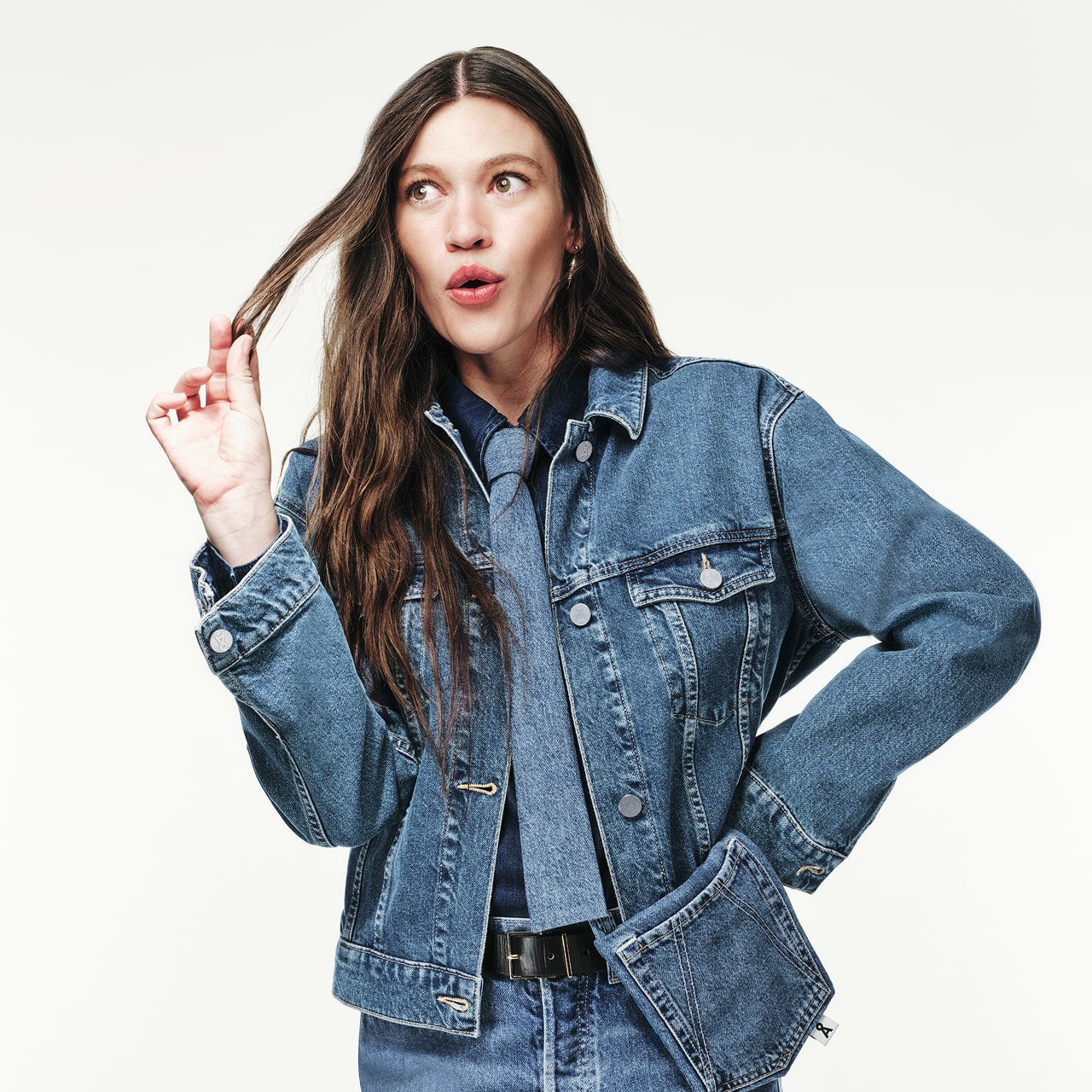 Person trägt Jeansjacke und Jeanshemd mit passender Krawatte, spielt mit einer Haarsträhne und blickt überrascht zur Seite.