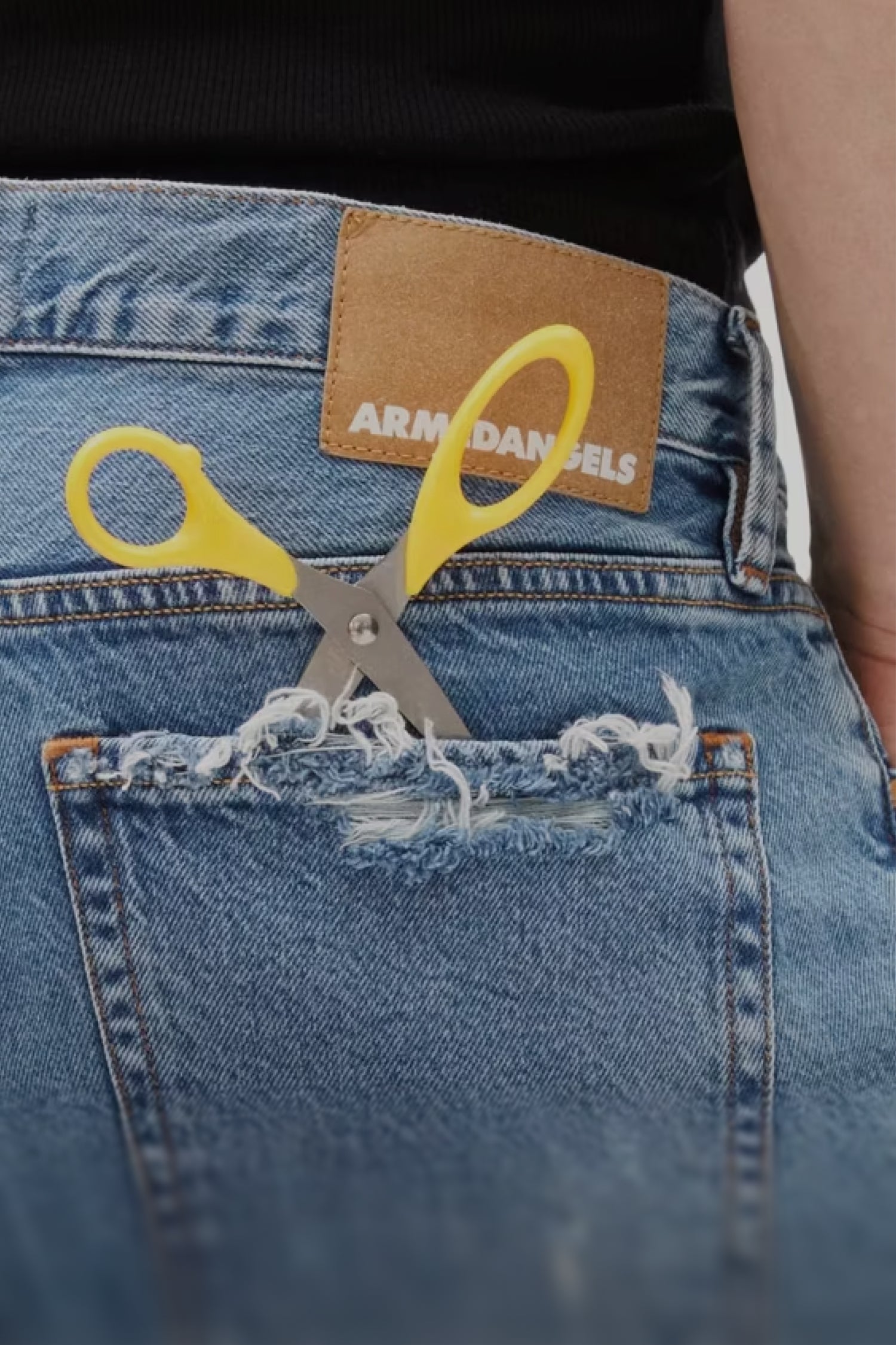 Jeans von hinten mit Fokus auf einer abgenutzten Jeanstasche mit Schere drinnen. Klicke hier um mehr über unseren Repair Service zu erfahren.