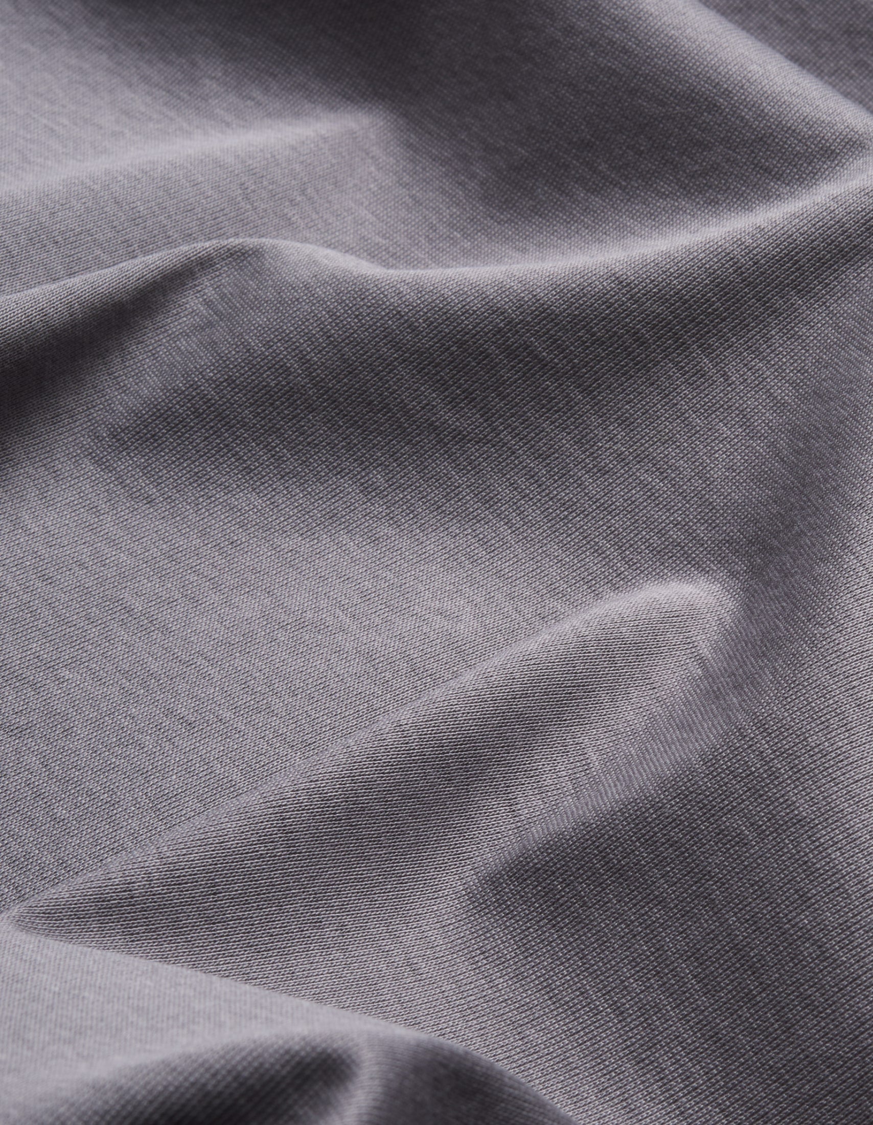 Nahaufnahme von grauem, leicht strukturiertem Stoff mit weichen Falten.