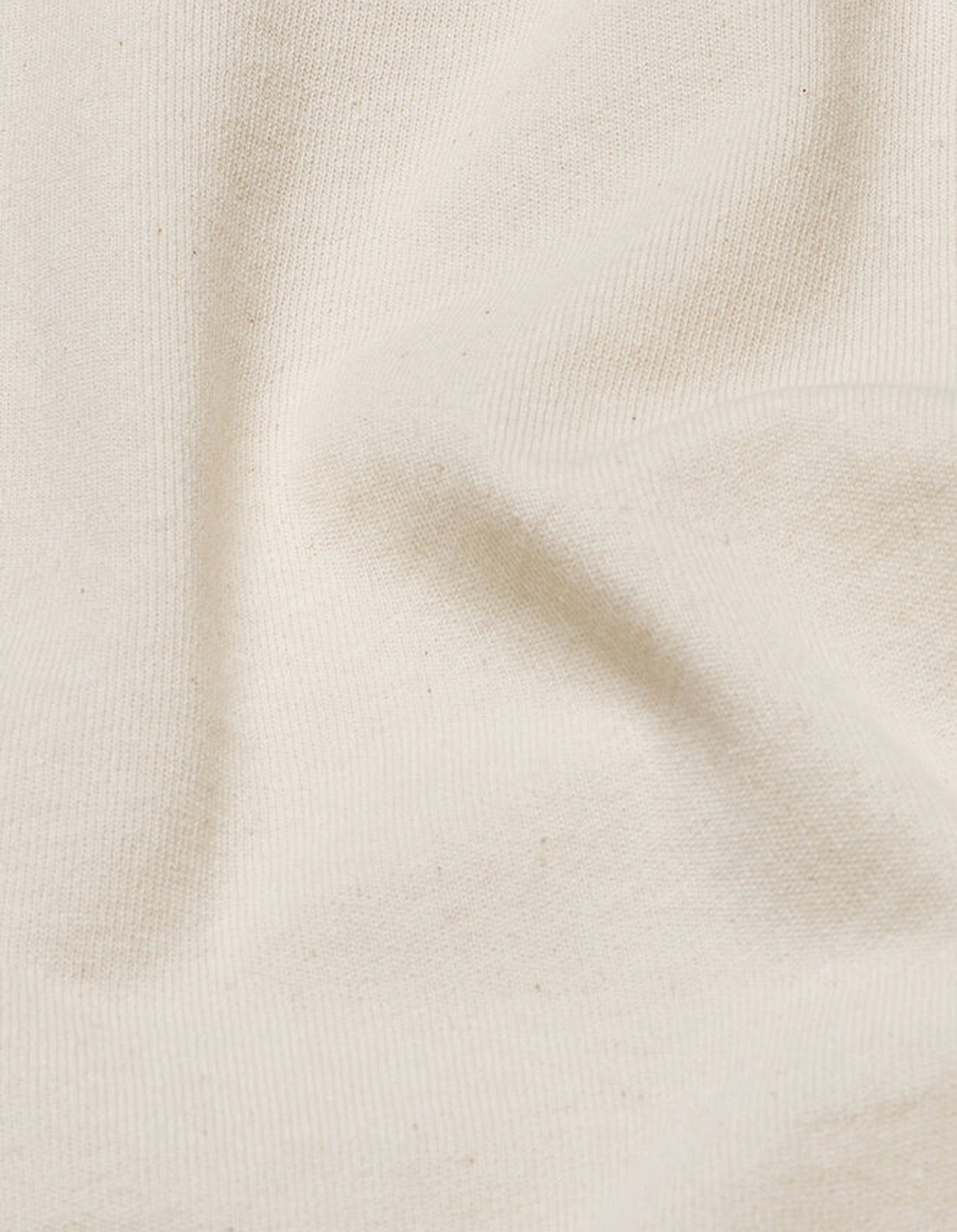 Nahaufnahme von cremefarbenem Stoff mit feiner Struktur und weichen Falten.