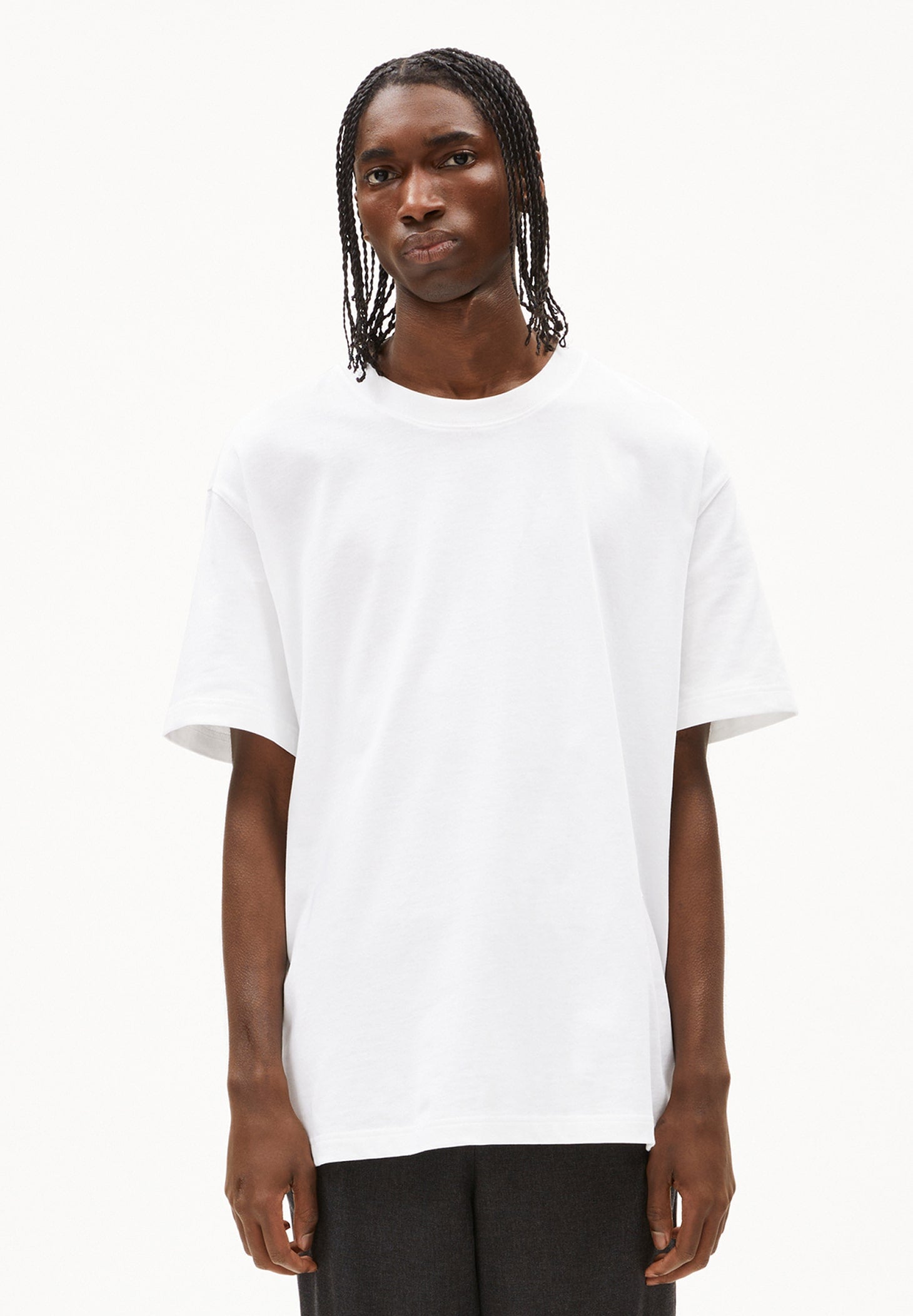 Person trägt weißes T-Shirt AADRU im Oversized Fit aus Bio-Baumwolle und dunkle Hose, frontal aufgenommen vor weißem Hintergrund.