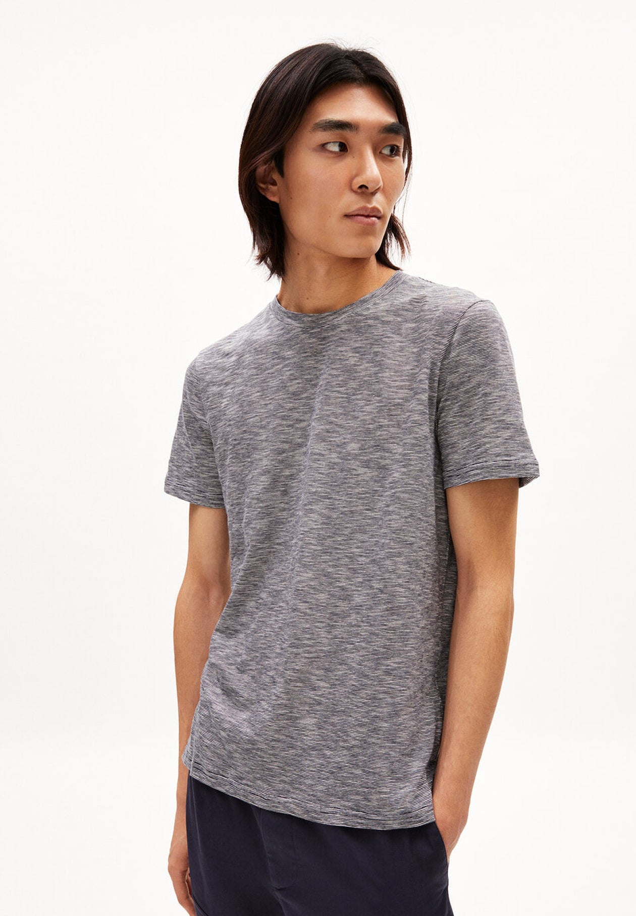 Person trägt grau meliertes T-Shirt JAAMES STRUCTURE im Regular Fit aus Bio-Baumwolle und dunkelblaue Hose, leicht seitlich aufgenommen vor weißem Hintergrund.