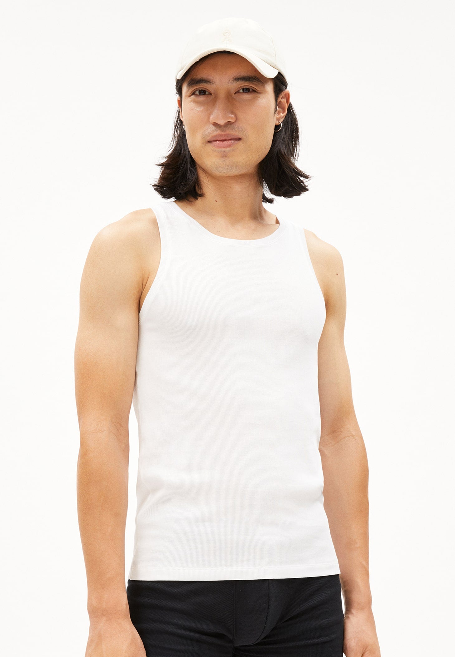 Person trägt weißes Ripp-Tanktop JAANNO RIB im Slim Fit aus Bio-Baumwolle und schwarze Hose, frontal aufgenommen vor weißem Hintergrund.