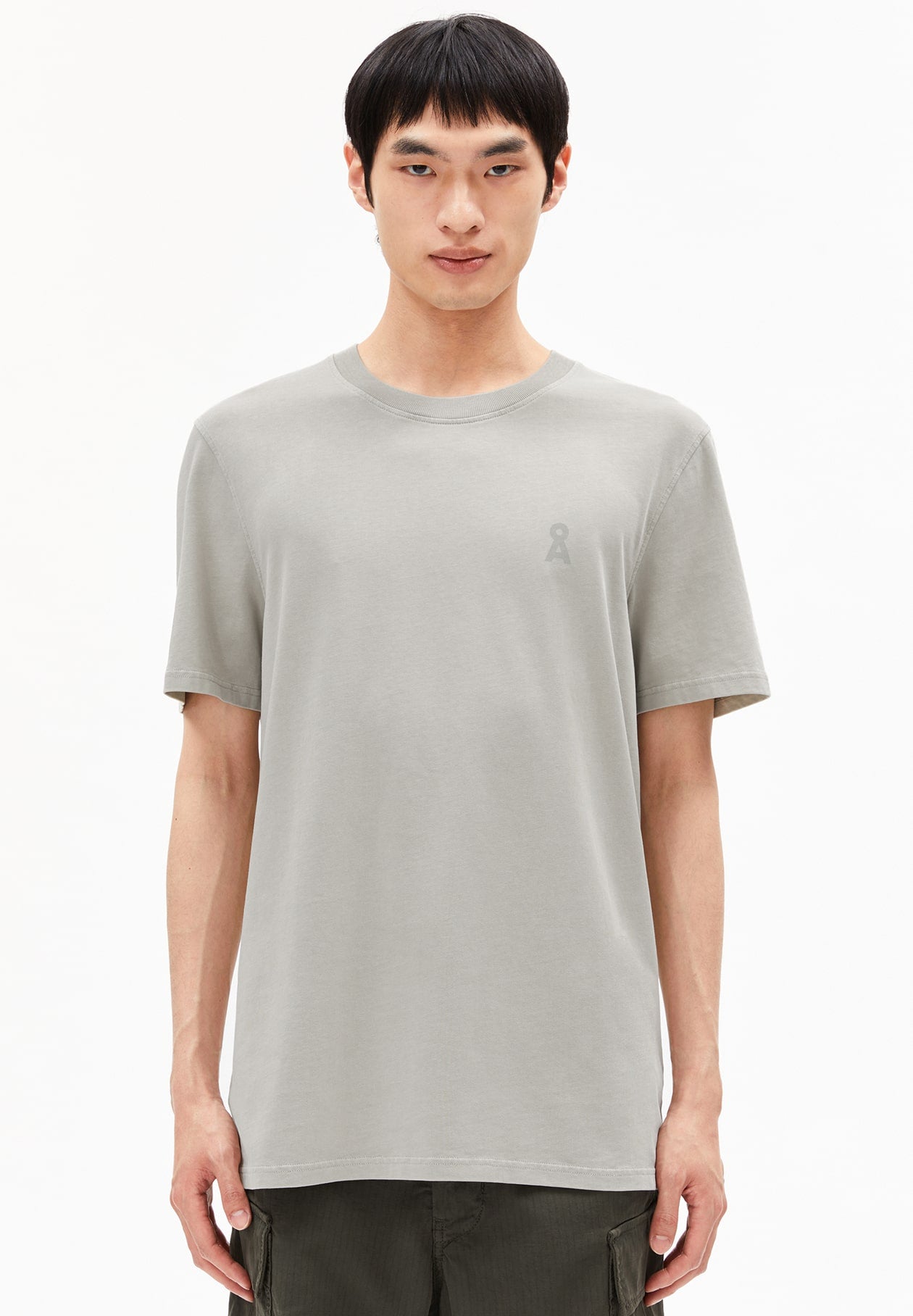 Person trägt graues T-Shirt ICONIC Å MAARKOS GMT DYE im Relaxed Fit mit kleinem Å-Logo auf der Brust und dunkelgrüne Hose, frontal aufgenommen vor weißem Hintergrund.