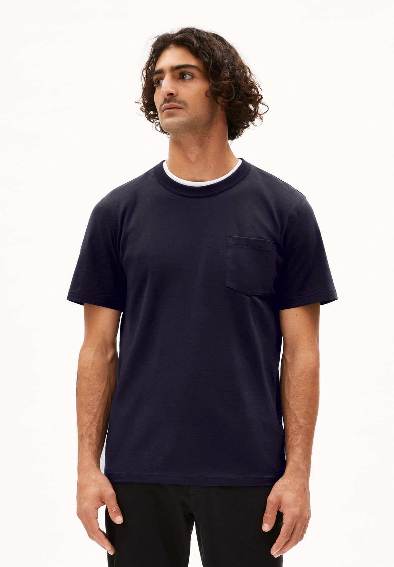 Person trägt dunkelblaues T-Shirt MAARKOS POCKET im Relaxed Fit mit Brusttasche und schwarze Hose, leicht seitlich aufgenommen vor weißem Hintergrund.