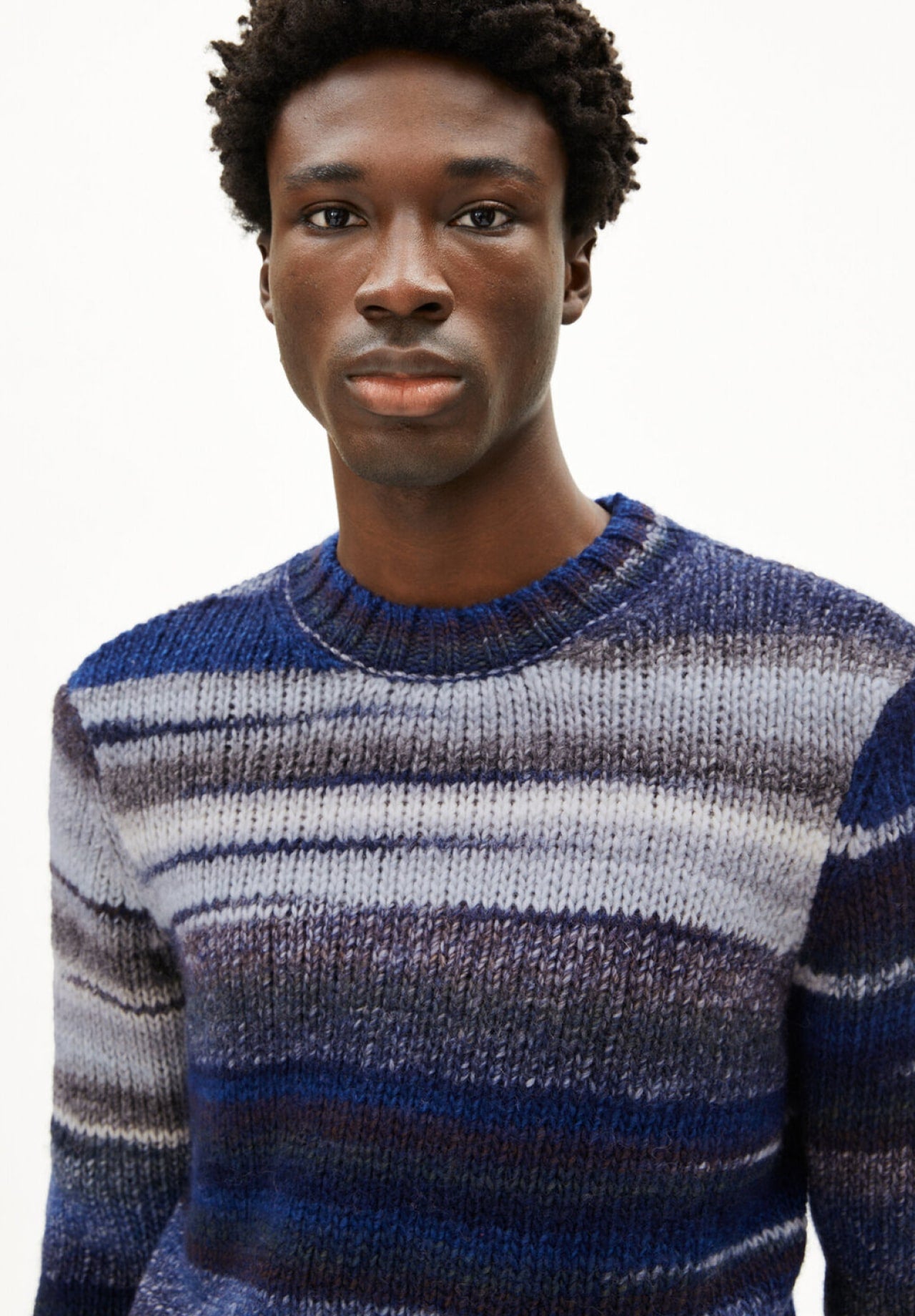 Person trägt einen grob gestrickten Pullover mit blauen und grauen Streifen.