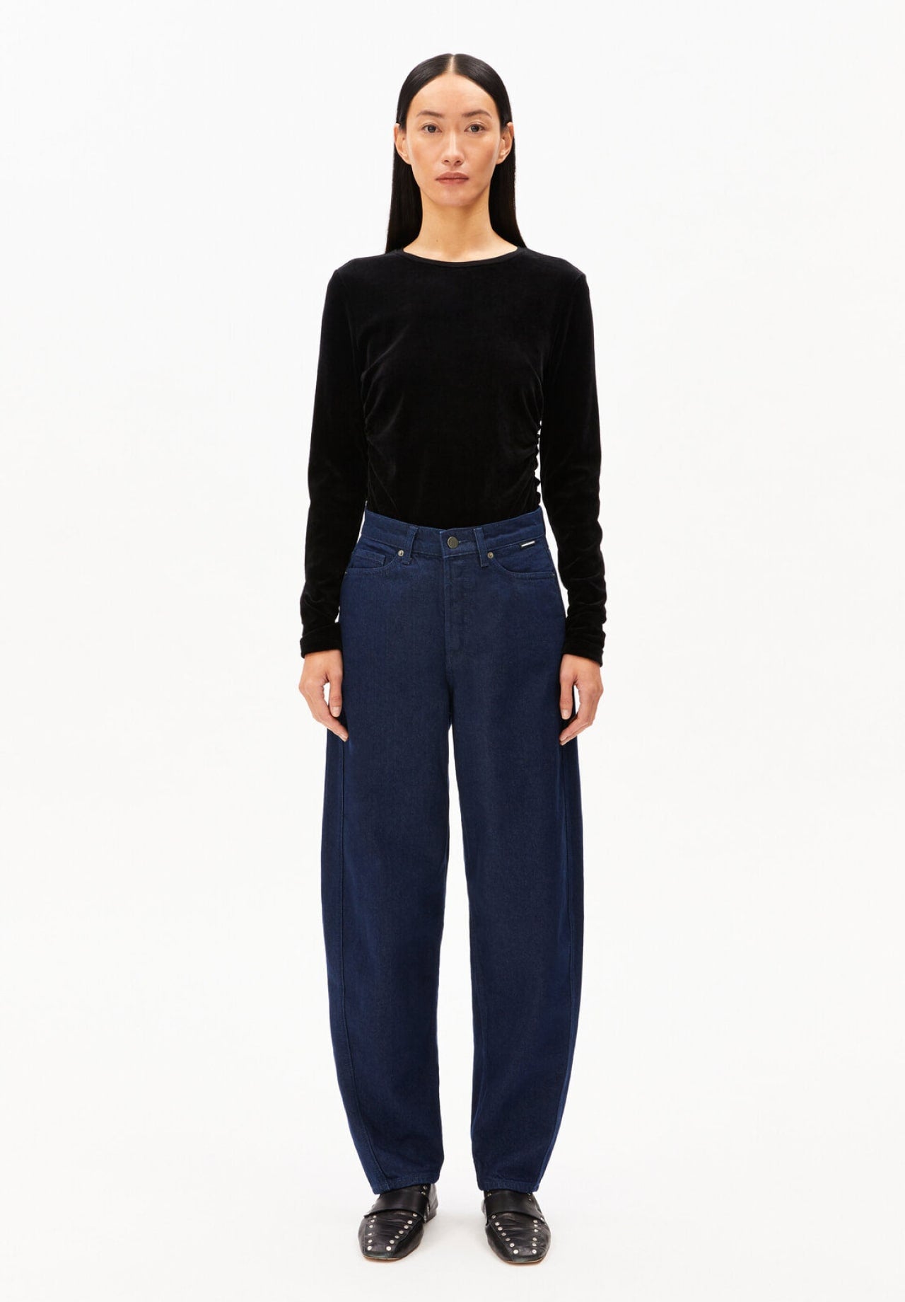Person trägt ein schwarzes Langarmshirt aus Samt und eine dunkelblaue, locker geschnittene Jeans.