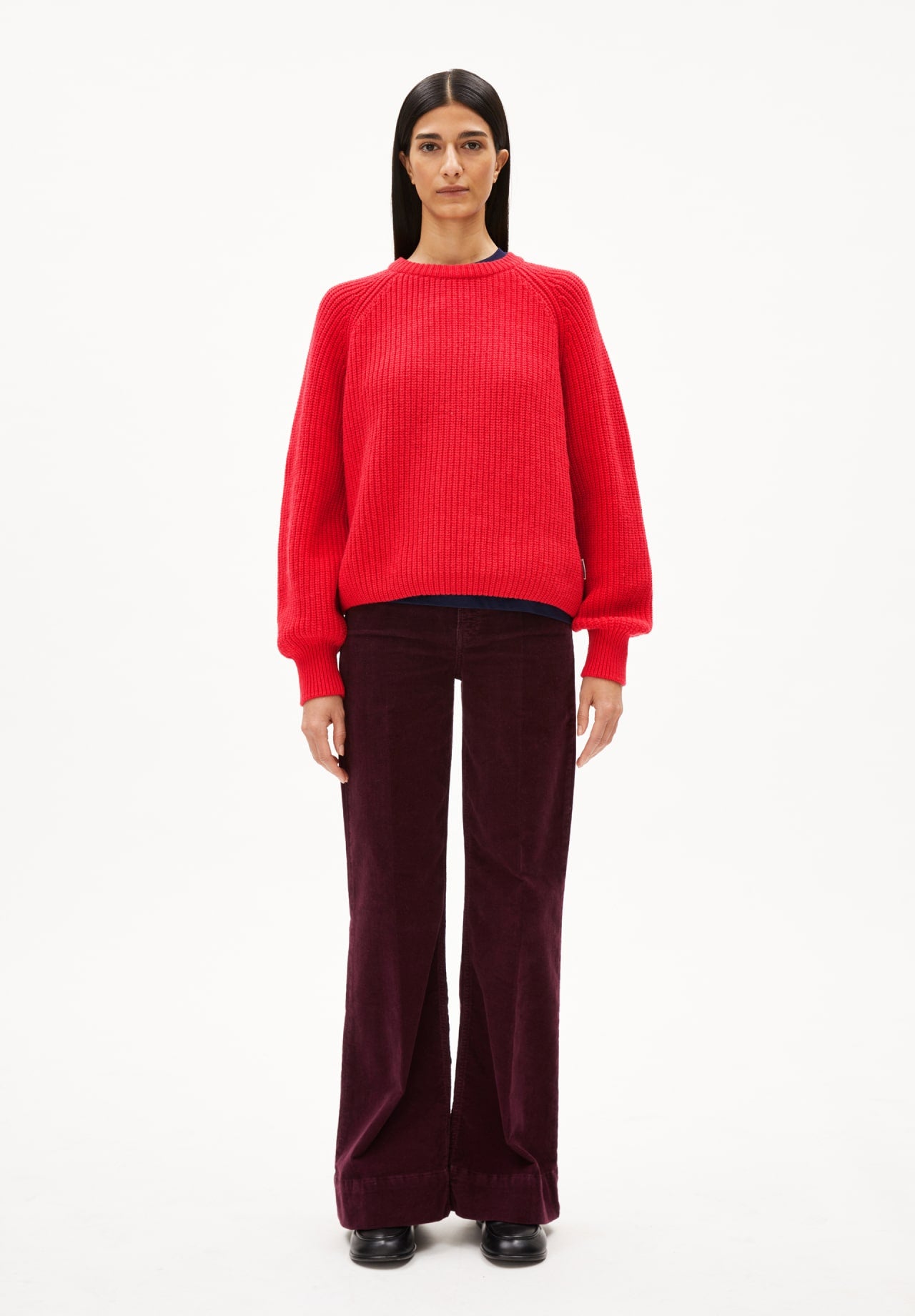 Person trägt einen roten Strickpullover und eine weit geschnittene, dunkelrote Cordhose.