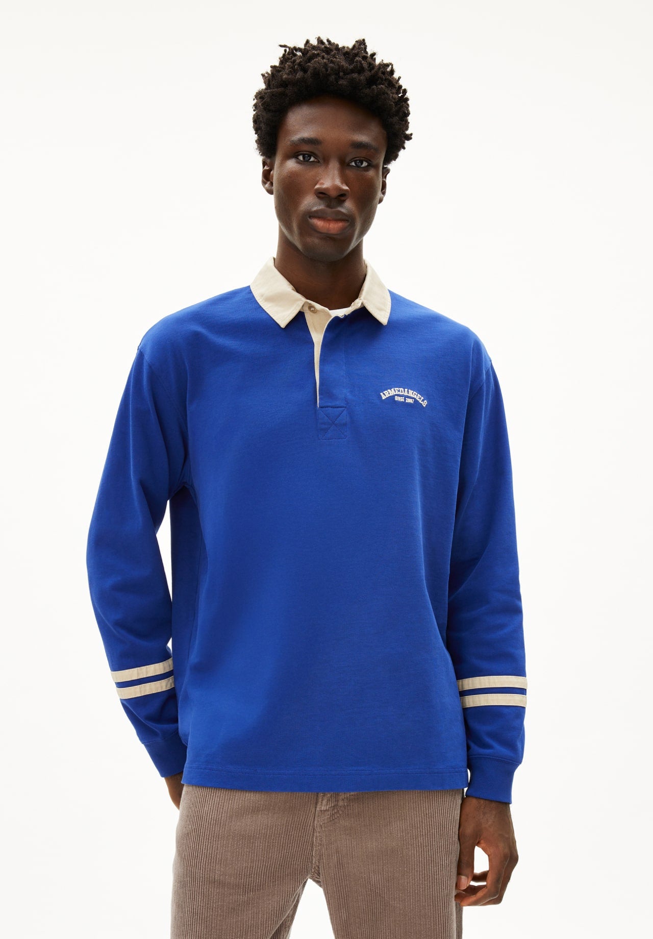 Person trägt ein blaues Langarmshirt mit Kragen und Logo und eine beige Cordhose.