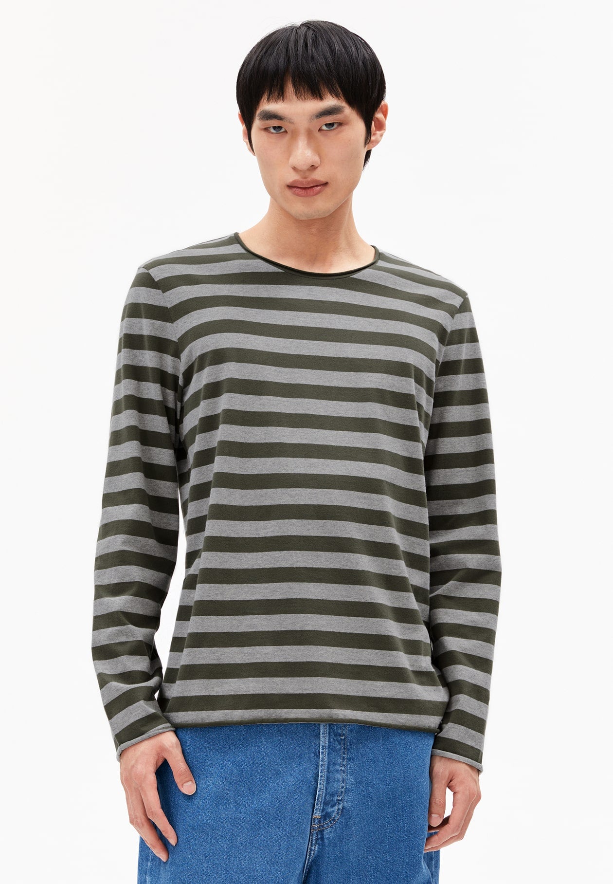 Mann guckt geradeaus und trägt das langärmlige MAARKOS LONGSLEEVE STRIPES T-Shirt in grün-grau gestreift. Dazu trägt er eine blaue Jeans. 