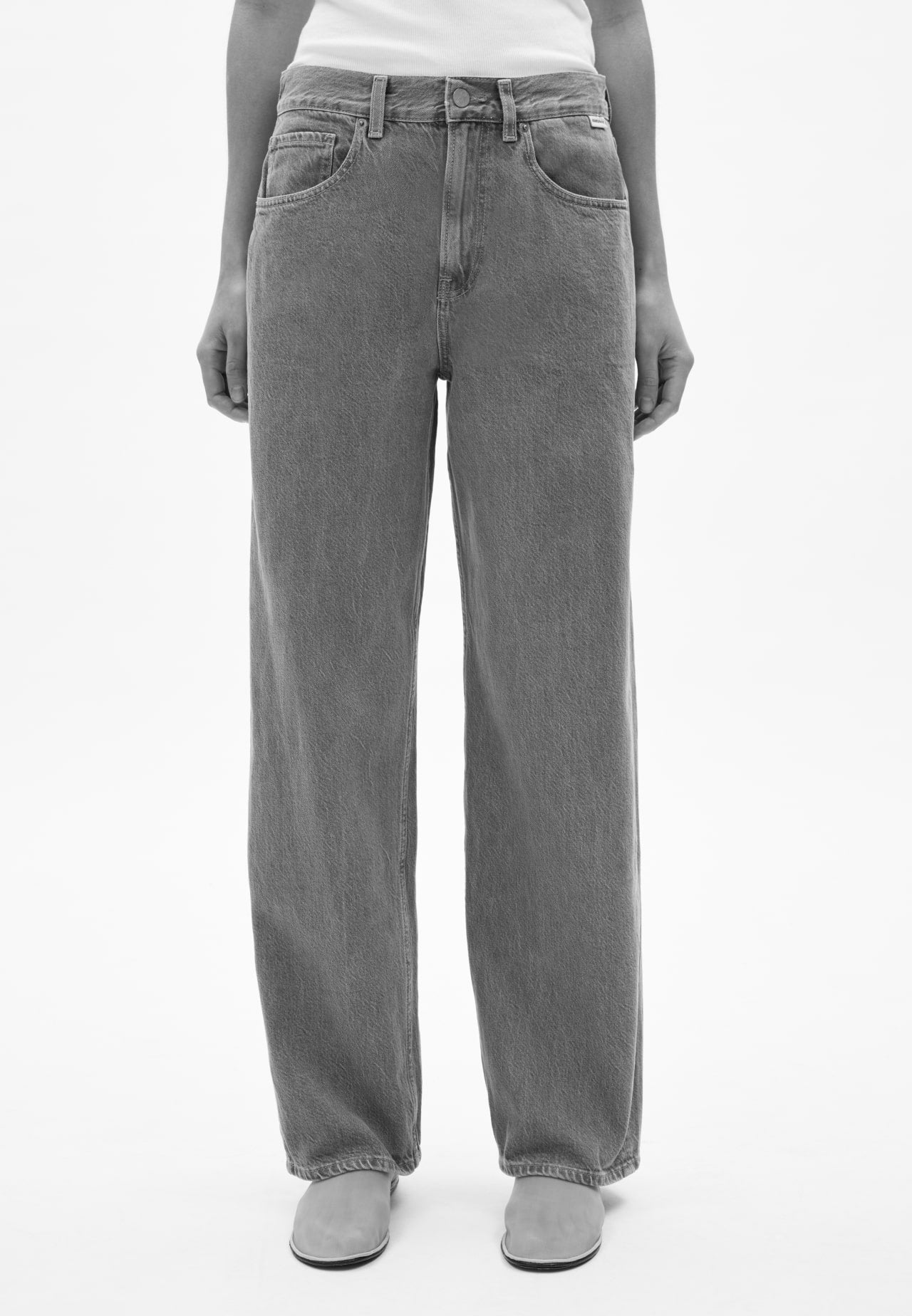 Vorderansicht einer Person mit blauer Jeans in geradem Schnitt, kombiniert mit weißem Oberteil und hellen Schuhen, vor hellem Hintergrund.