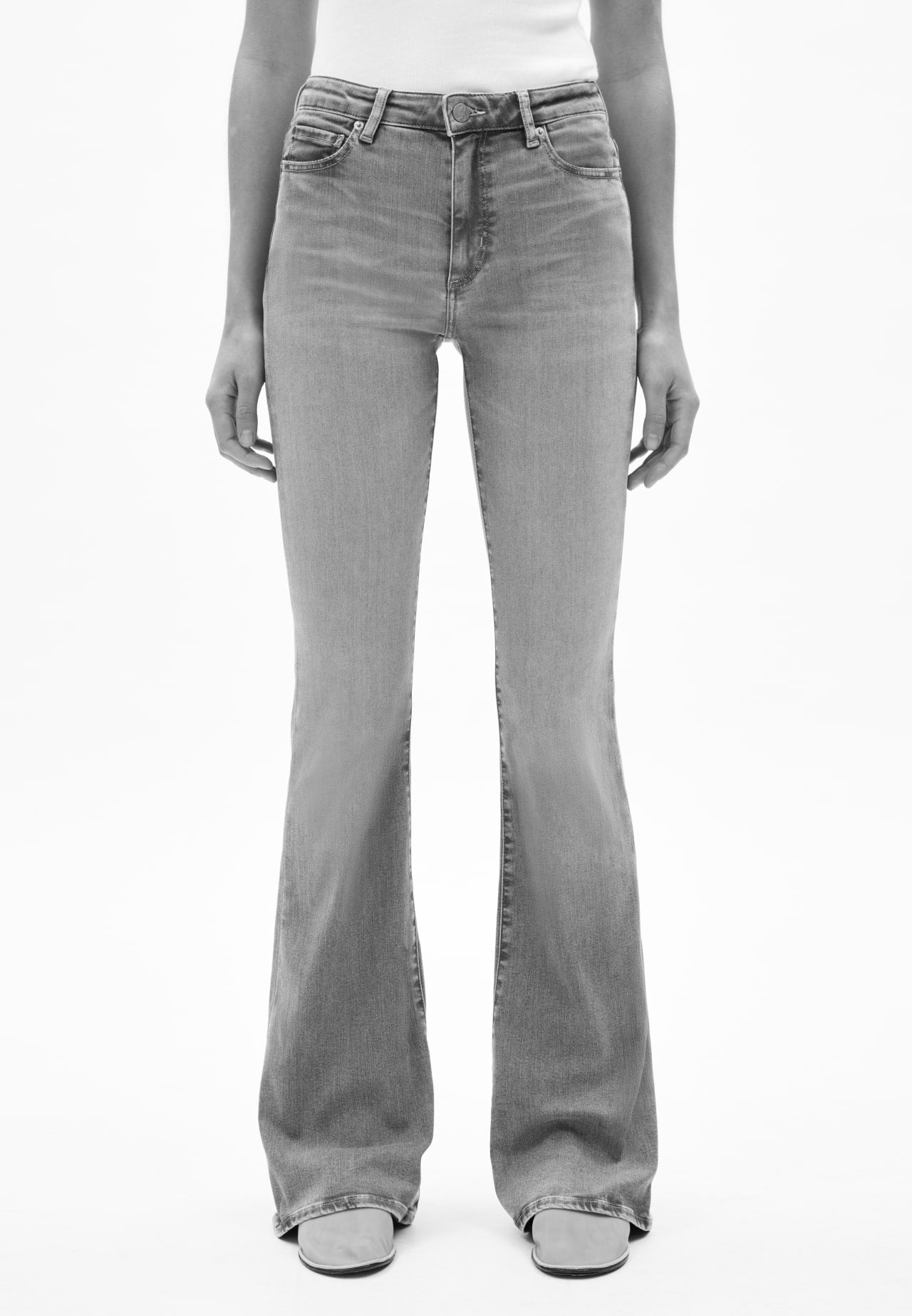 Vorderansicht einer Person mit blauer Jeans in geradem Schnitt, kombiniert mit weißem Oberteil und hellen Schuhen, vor hellem Hintergrund.