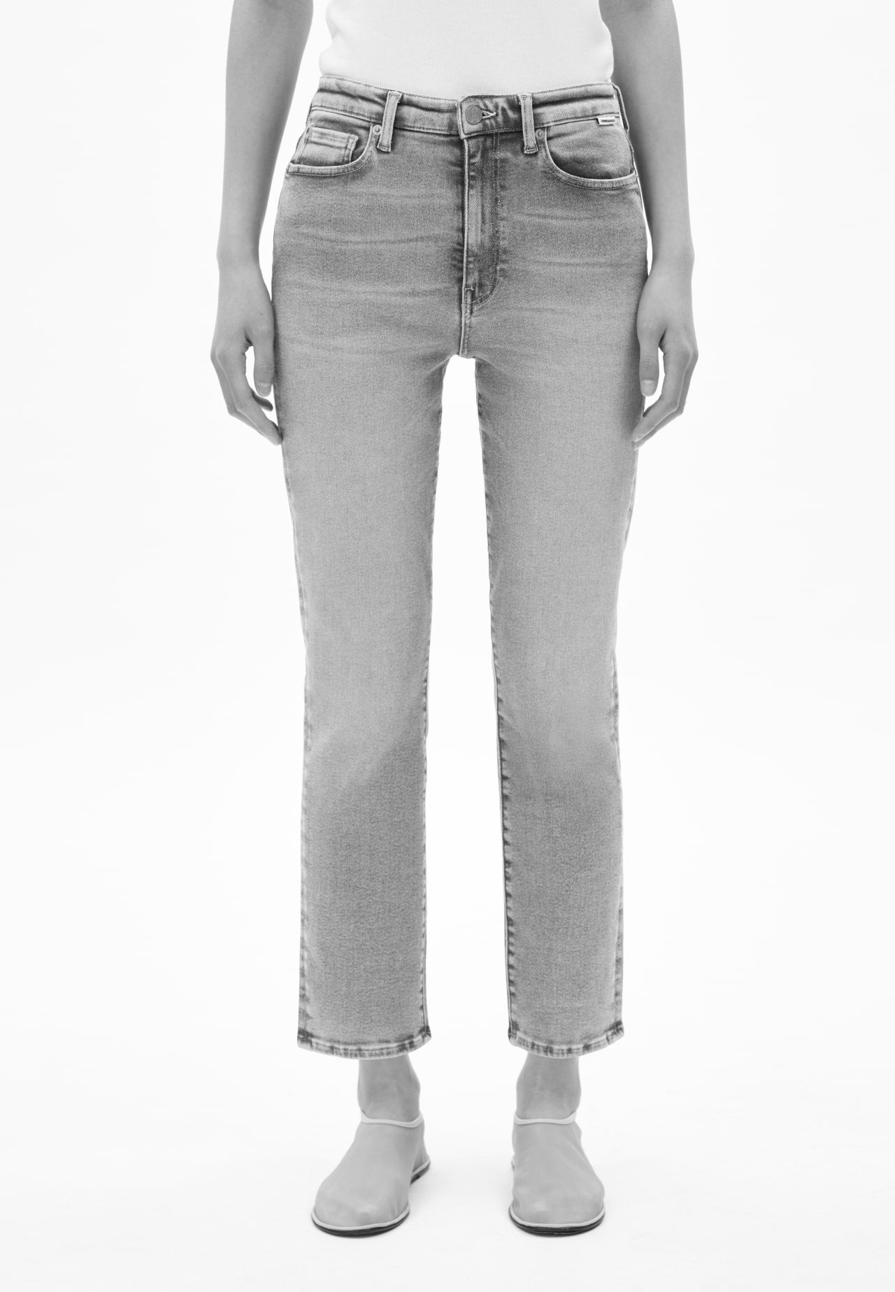 Vorderansicht einer Person mit blauer Jeans in geradem Schnitt, kombiniert mit weißem Oberteil und hellen Schuhen, vor hellem Hintergrund.