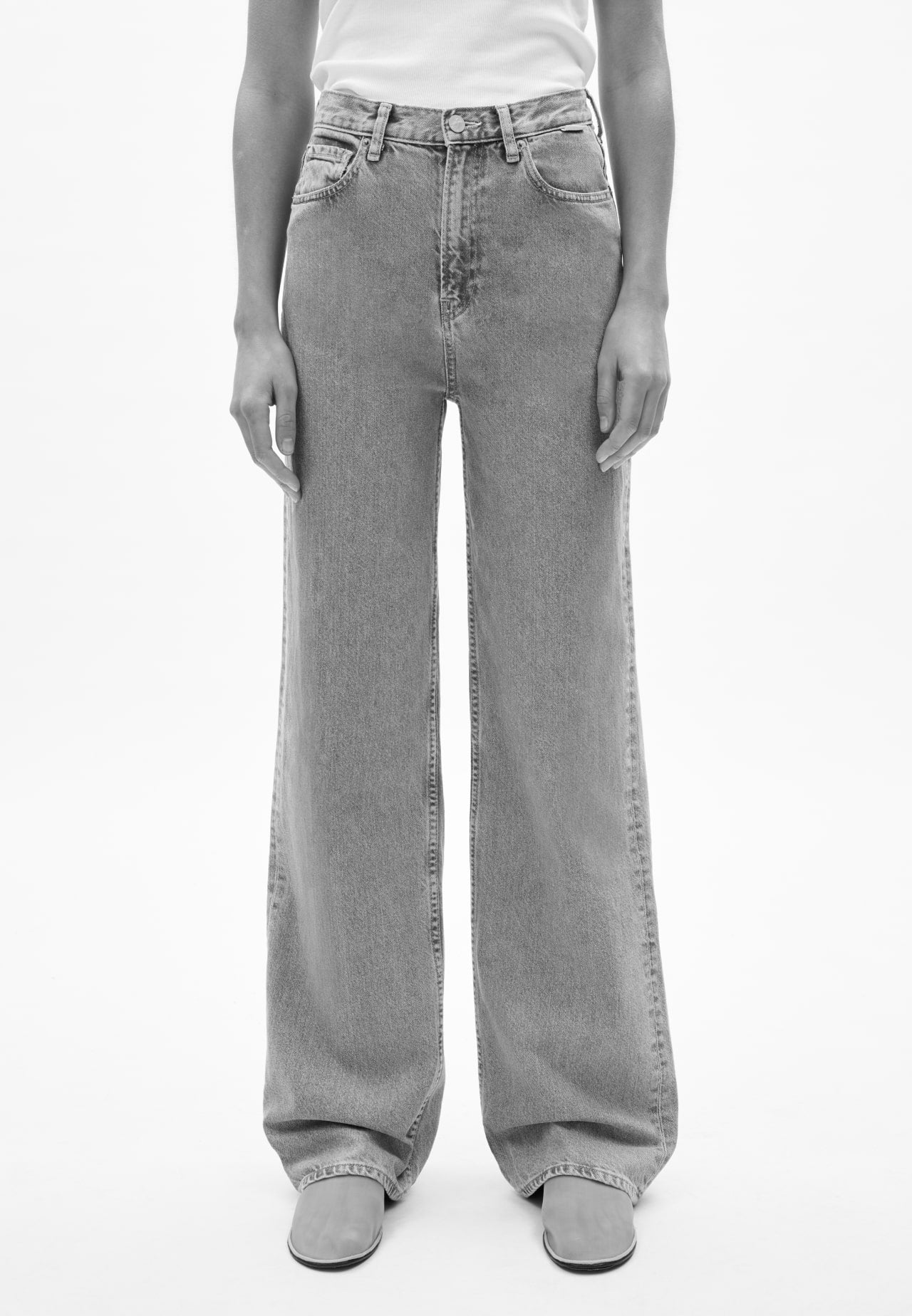 Vorderansicht einer Person mit blauer Jeans in geradem Schnitt, kombiniert mit weißem Oberteil und hellen Schuhen, vor hellem Hintergrund.