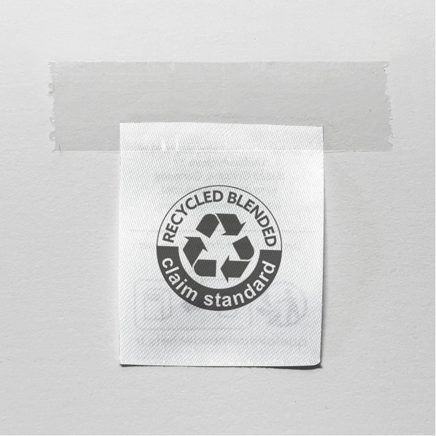 Etikett mit Recycling-Symbol und Aufschrift „Recycled Blended – Claim Standard“, an eine Wand geklebt.