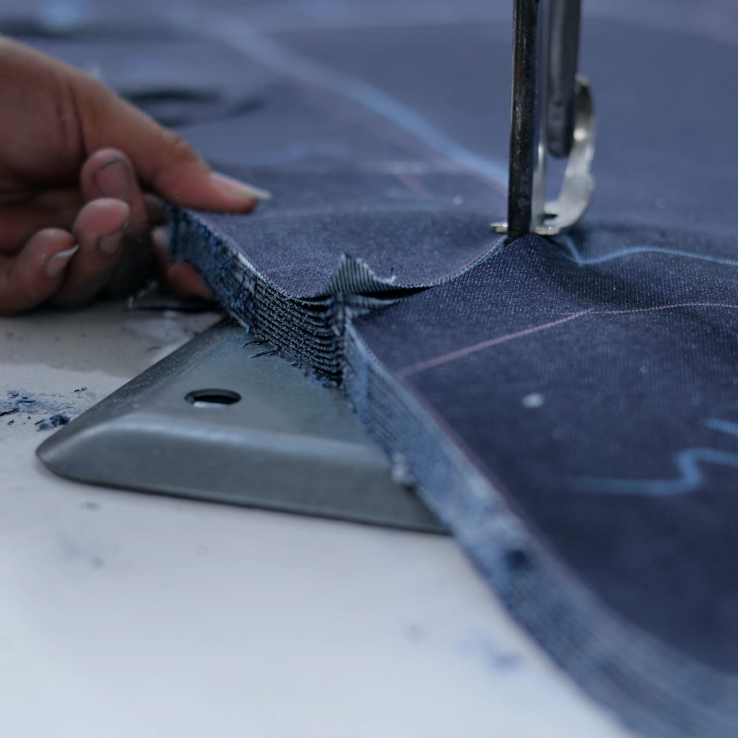 Nahaufnahme einer Nähmaschine, die mehrere Lagen Denimstoff zusammennäht, gehalten von einer Hand.