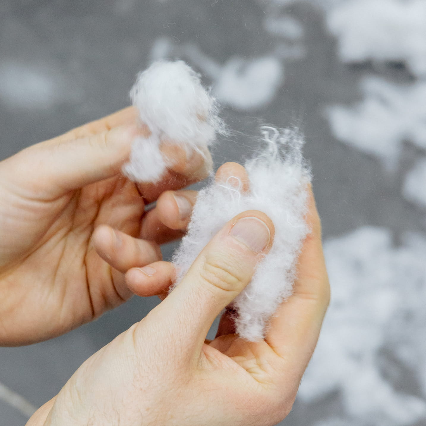 Hände halten weiche, weiße Recyclingfasern aus zerkleinerten Textilien.