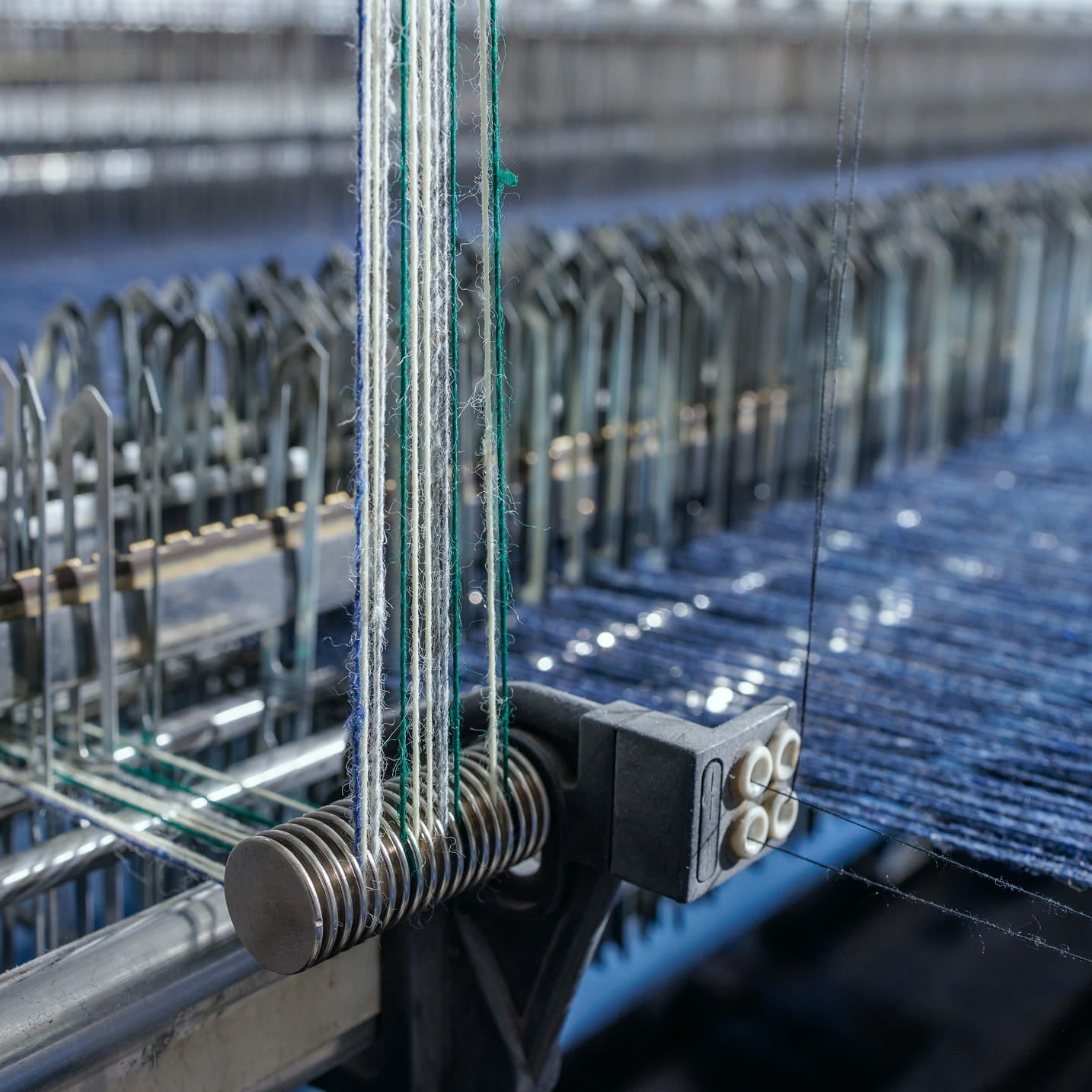 Detailaufnahme eines Webstuhls mit gespannten Garnen und laufendem Denimgewebe.