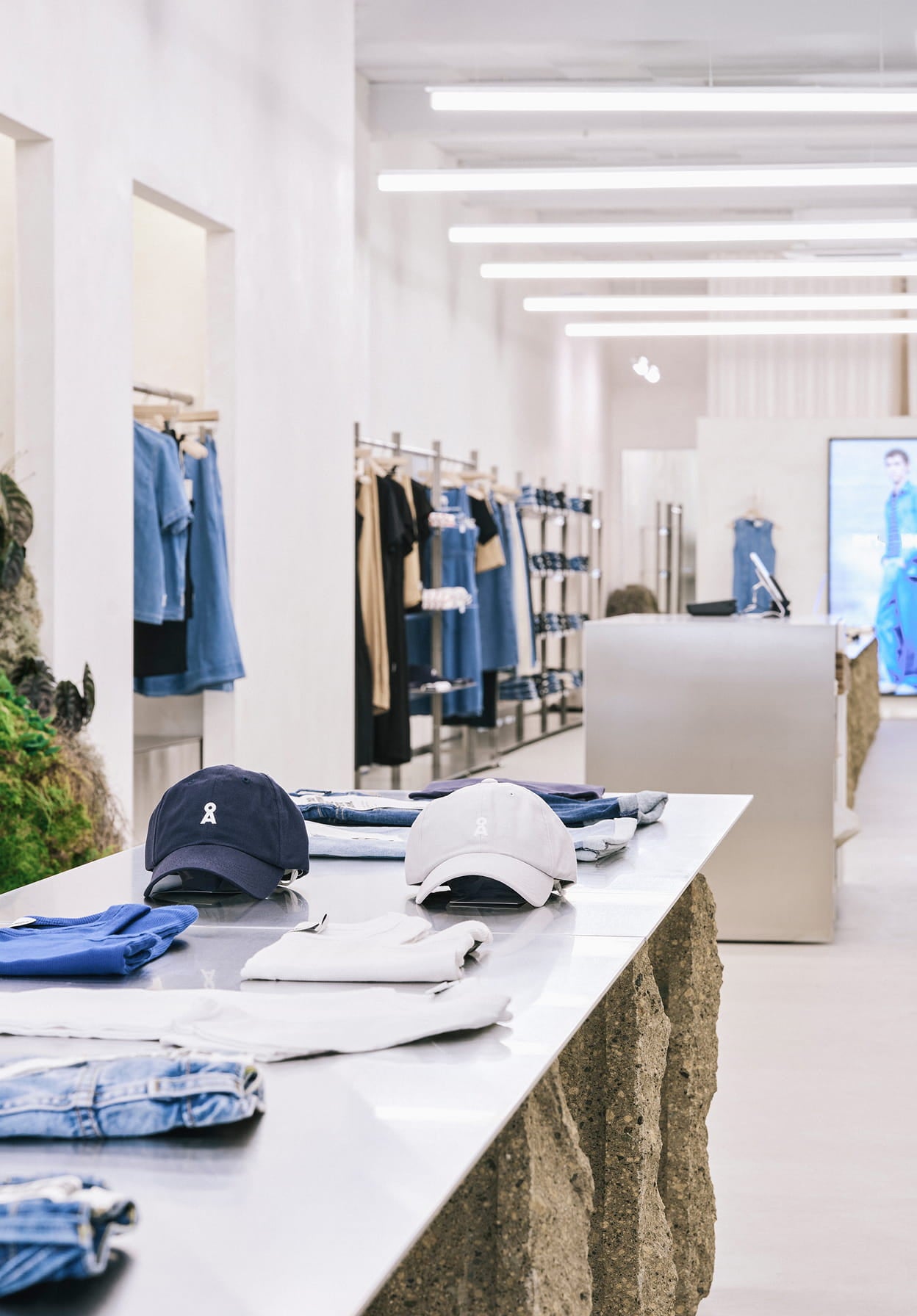 Minimalistisch gestalteter Store mit gefalteter Denim- und Casualwear sowie Caps auf einem zentralen Präsentationstisch.