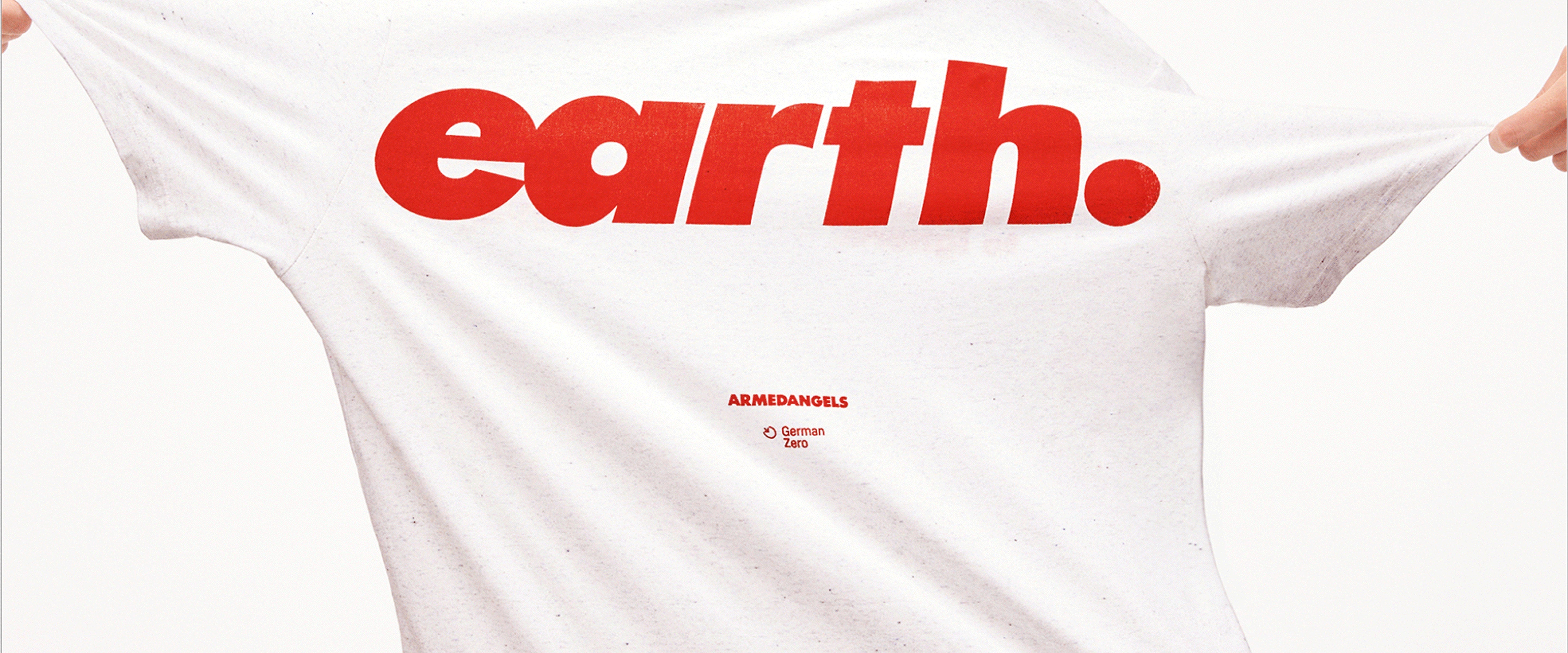 Nahaufnahme eines weißen T-Shirts mit großem roten Schriftzug ‚earth.‘ und kleinem Armedangels-Logo darunter; das Shirt wird seitlich gespannt gehalten.