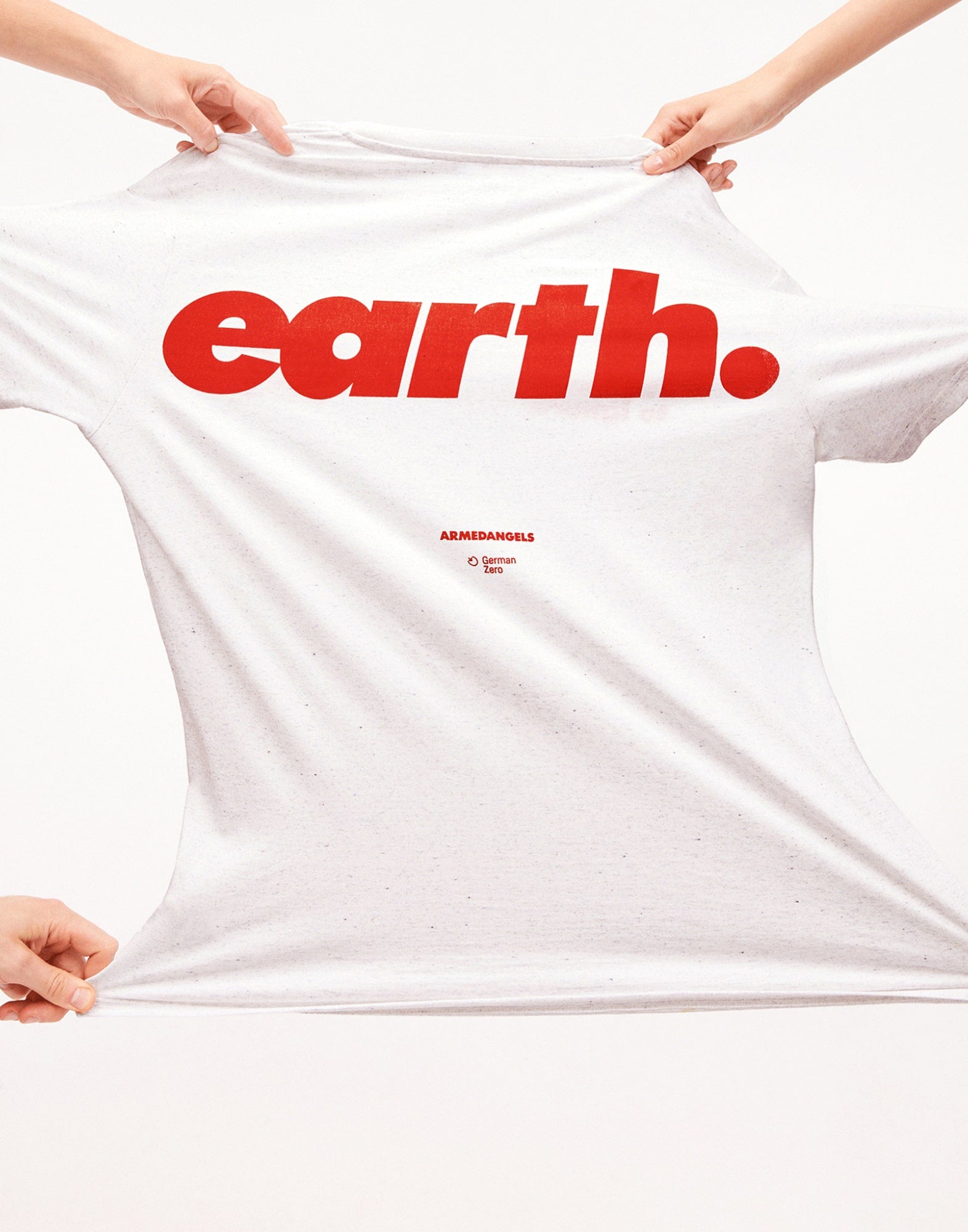 Nahaufnahme eines weißen T-Shirts mit großem roten Schriftzug ‚earth.‘ und kleinem Armedangels-Logo darunter; das Shirt wird seitlich gespannt gehalten.