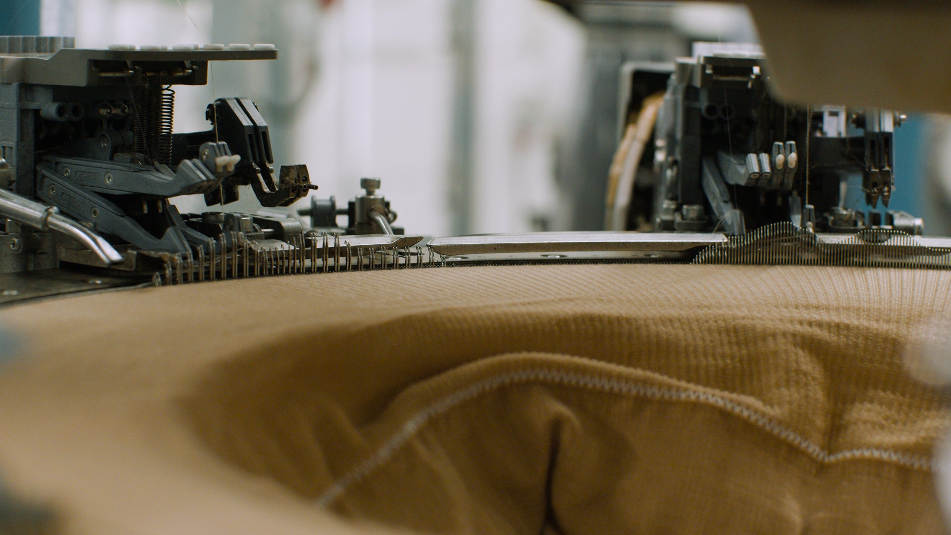 Nahaufnahme einer Strickmaschine, die beigefarbenen Stoff verarbeitet.