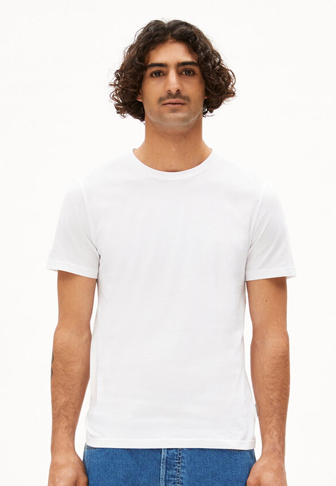Person trägt schlichtes weißes Regular Fit T-Shirt aus Bio-Baumwolle und blaue Jeans, frontal aufgenommen vor weißem Hintergrund.