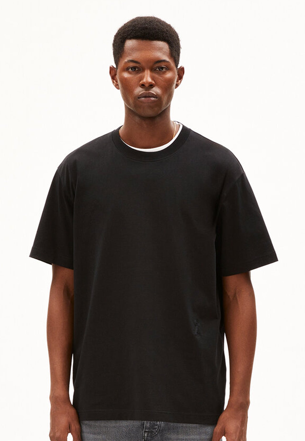 Model trägt schwarzes oversized T-Shirt aus Bio-Baumwolle und graue Jeans, frontal aufgenommen vor weißem Hintergrund.