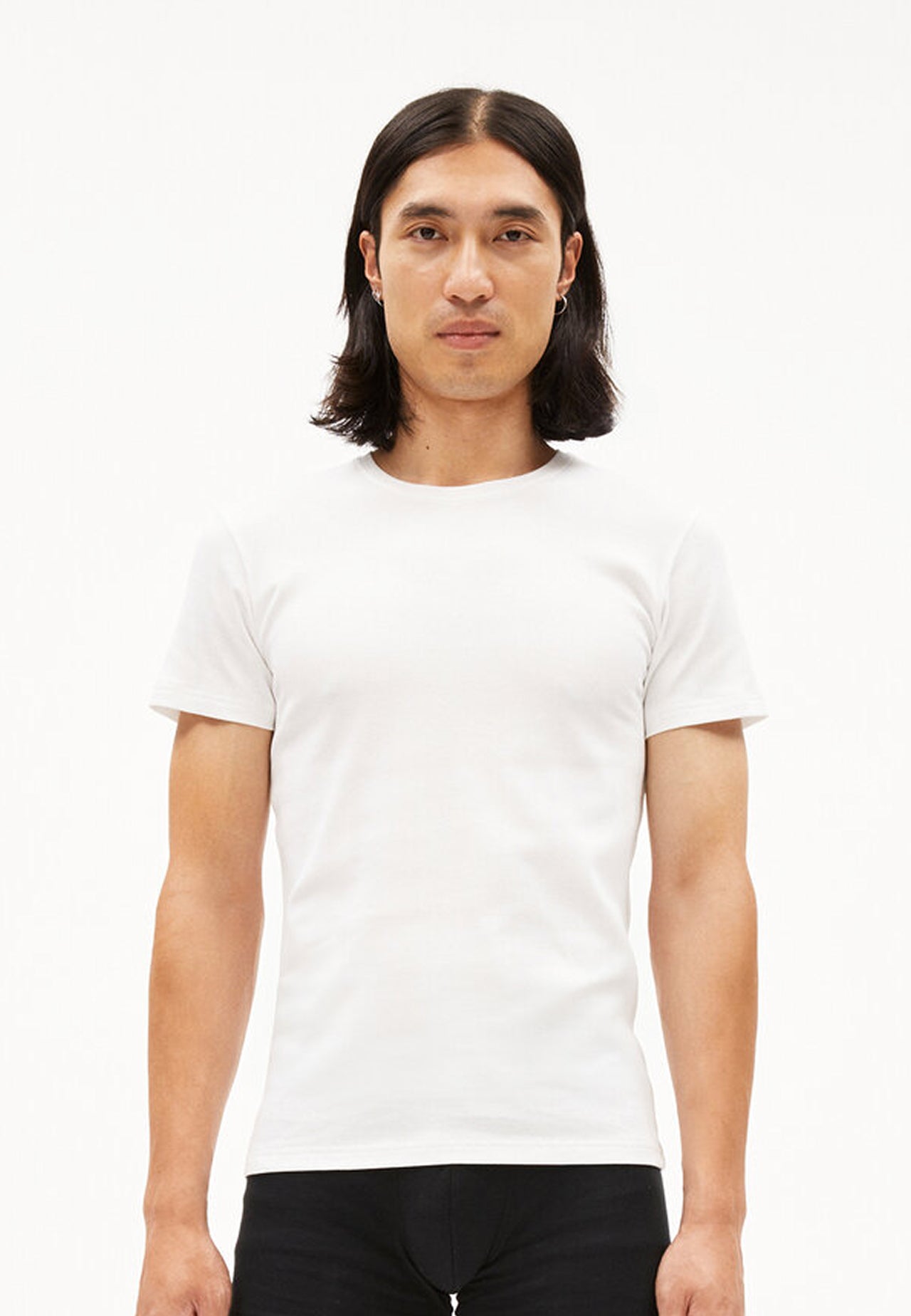 Model trägt weißes slim-fit T-Shirt aus Bio-Baumwolle und schwarze Hose, frontal aufgenommen vor weißem Hintergrund.